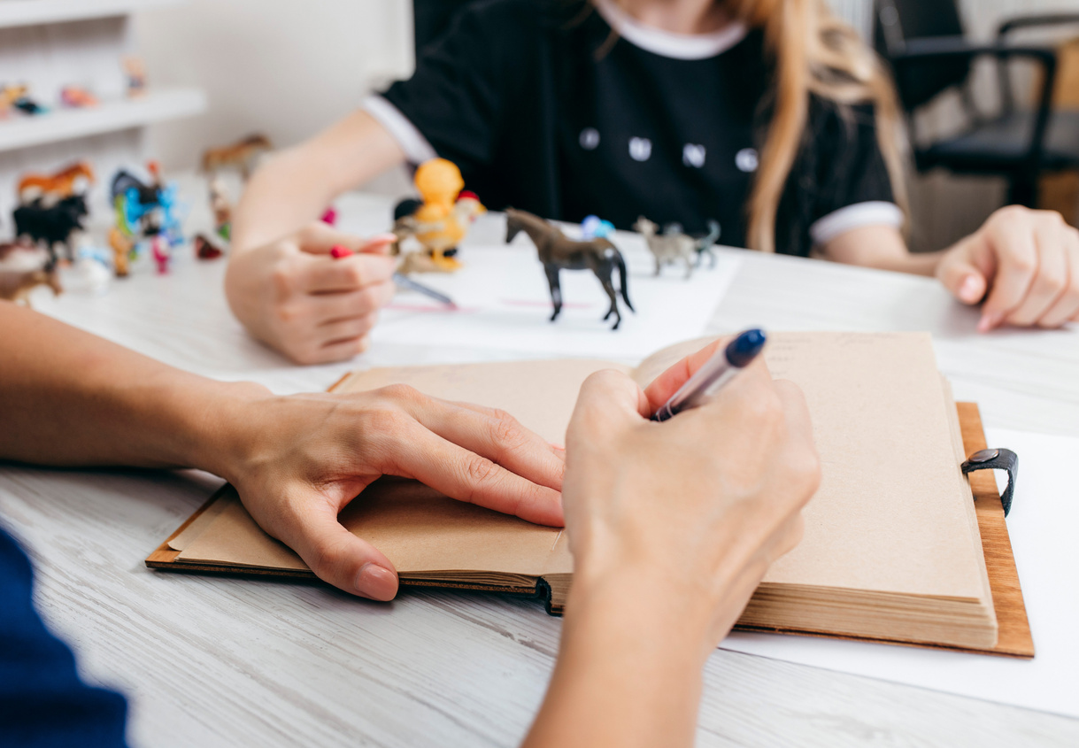 Professional child psychologist with a teenage girl. Psychologist makes notes in a notebook